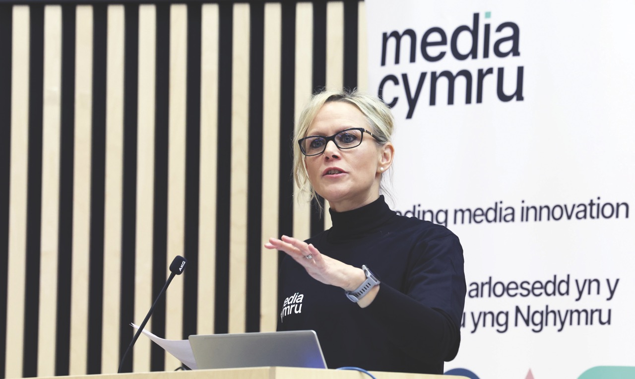 A woman standing at a lectern and presenting at a Media Cymru event