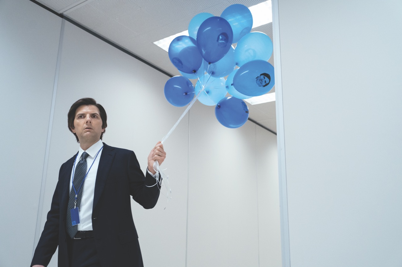 A still from Severance showing a man in a suit carrying a bunch of blue balloons down a hallway