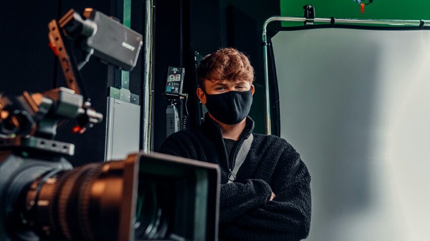 ScreenSkills offers development programmes for professionals to build upon their skillsets A young man wearing a mask and standing in a studio next to a professional camera