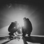 A black and white photo of two men kneeling down with a professional camera