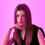 A model resting her chin on her hand in pink lighting