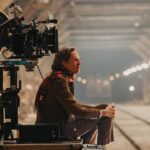 Side view of a man sitting next to a large camera in a tunnel with tracks running through the centre