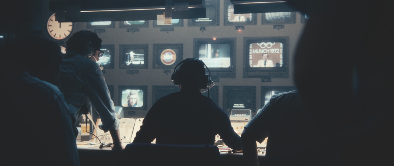 People in silhouette facing a wall of screens in a film studio