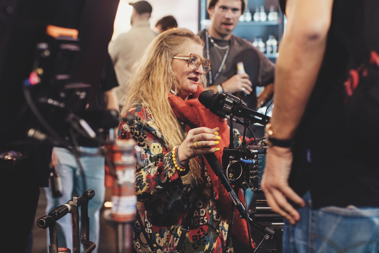 A woman in bright clothes operating a professional camera at a busy conference