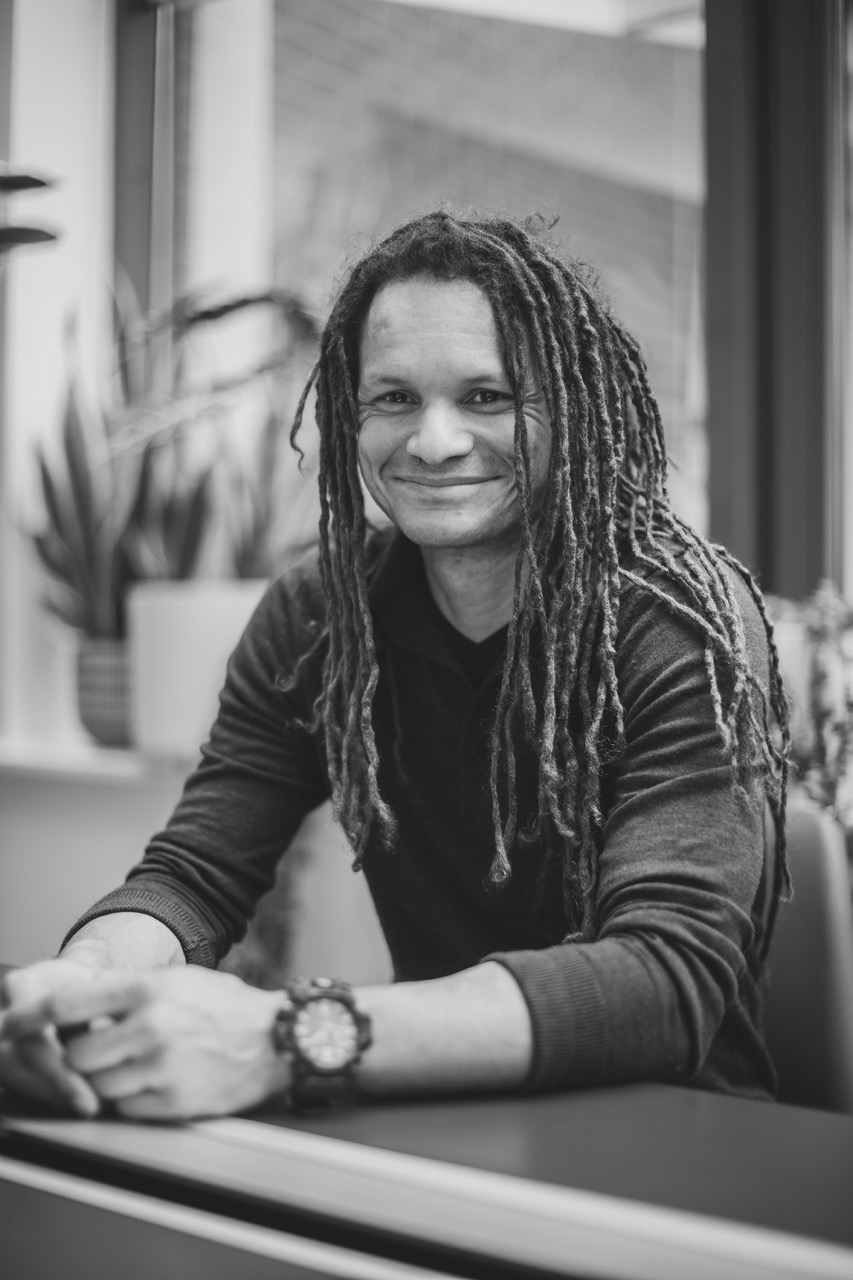 A black and white still of a smiling man in an office space