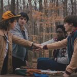 A still from Stranger Things showing a group of young boys standing in an autumnal wood with their hands together