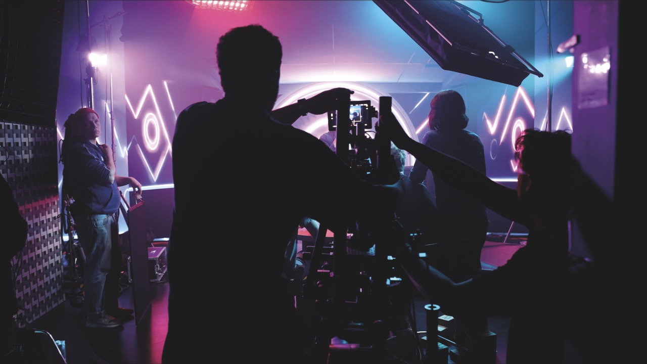 processed-C50F4279-1CCB-4EBD-9A82-E414AD0CDAAE Large Silhouettes of people adjusting camera equipment with bright lights behind